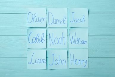 Photo of Paper notes with different baby names on light blue wooden table, flat lay