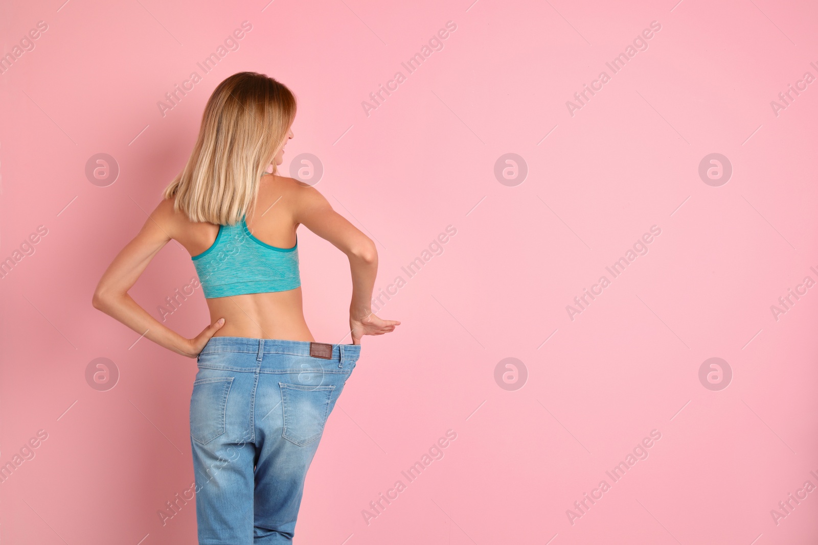 Photo of Young slim woman in old big jeans showing her diet results on color background