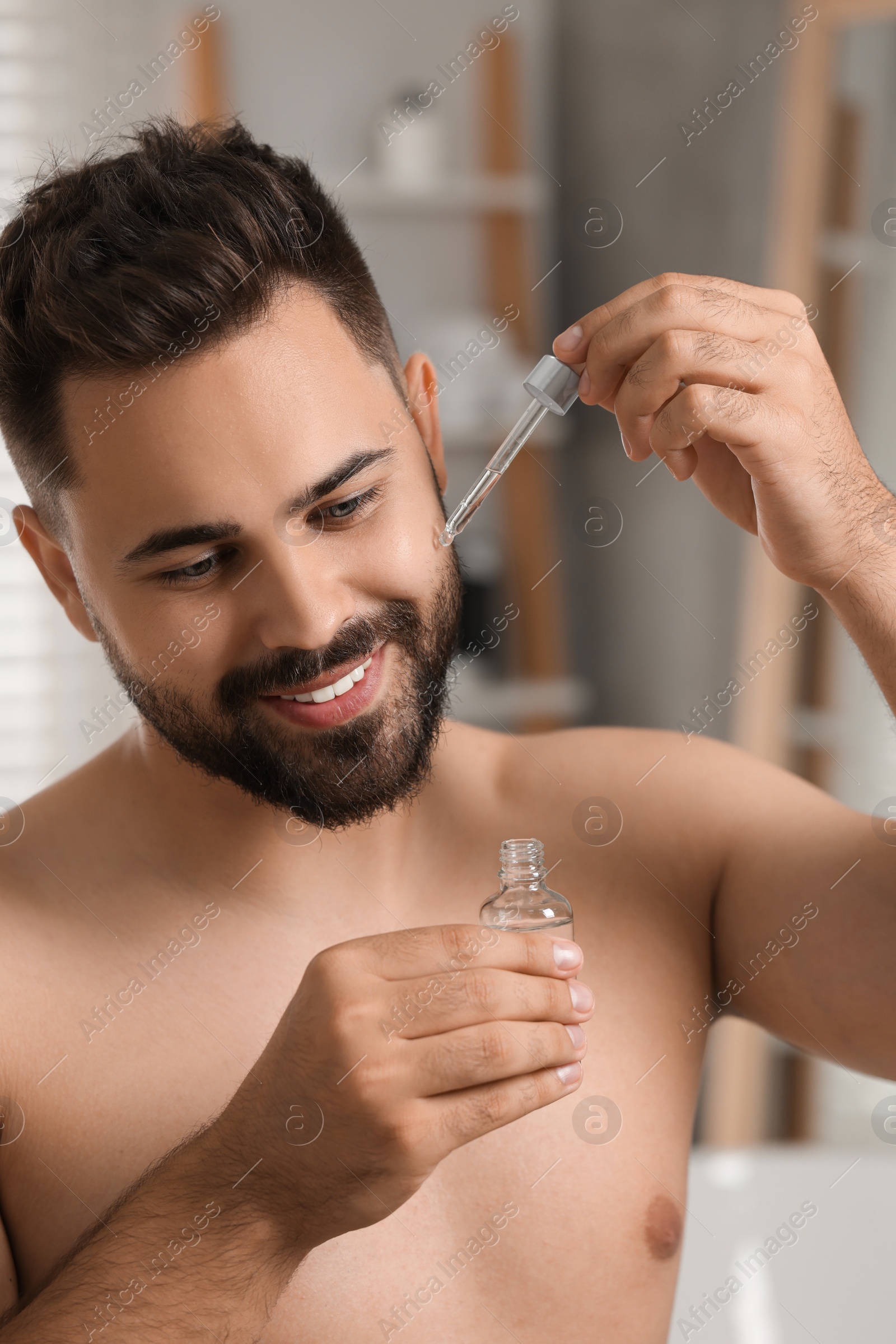 Photo of Handsome man applying cosmetic serum onto his face in bathroom