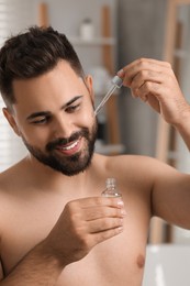 Photo of Handsome man applying cosmetic serum onto his face in bathroom