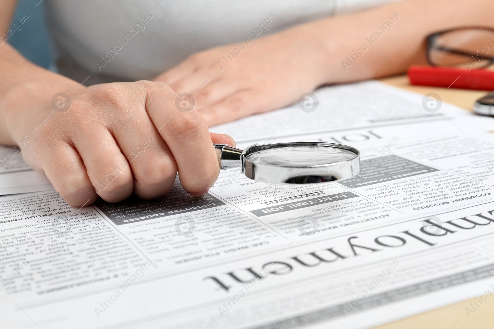 Photo of Woman looking through magnifying glass at newspaper, closeup. Job search concept