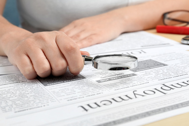 Woman looking through magnifying glass at newspaper, closeup. Job search concept