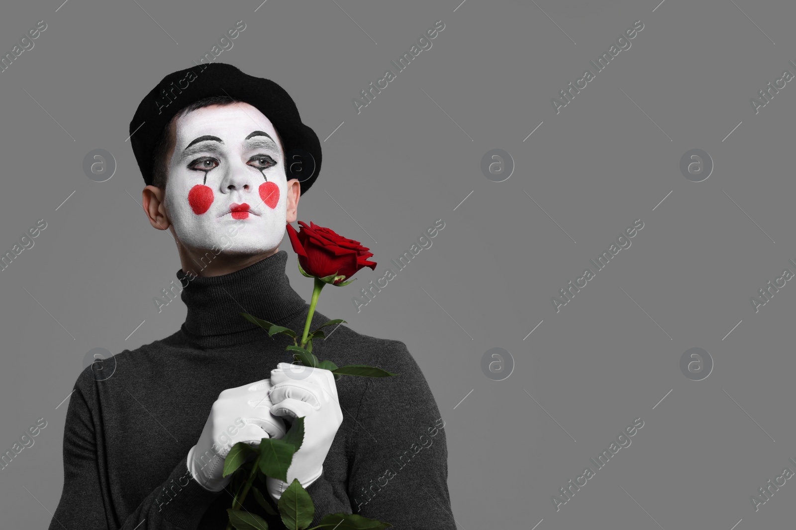 Photo of Portrait of mime artist with red rose on grey background. Space for text