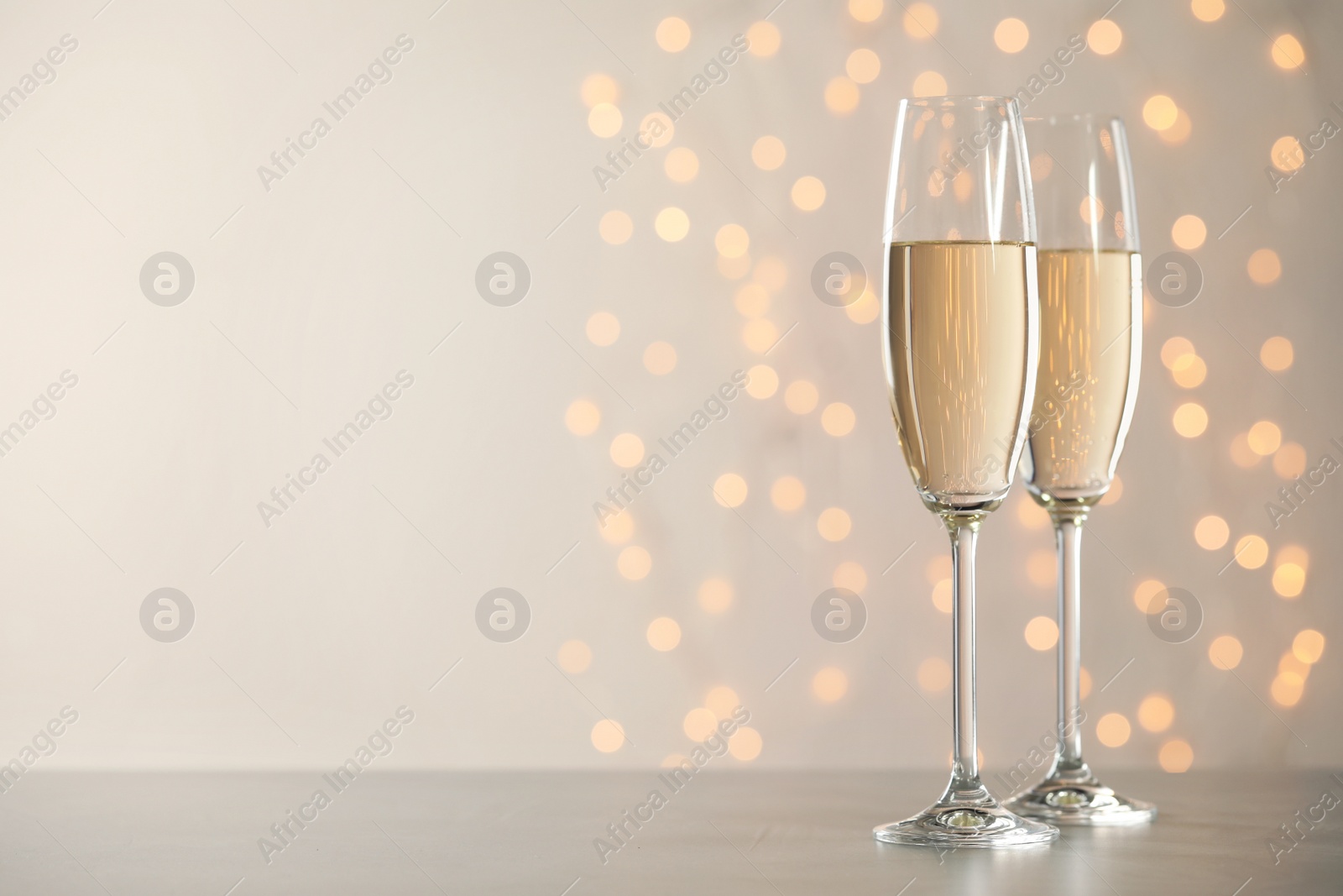 Photo of Glasses of champagne on grey table against blurred lights. Space for text