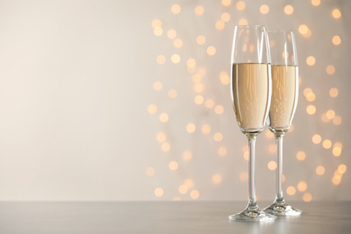Photo of Glasses of champagne on grey table against blurred lights. Space for text