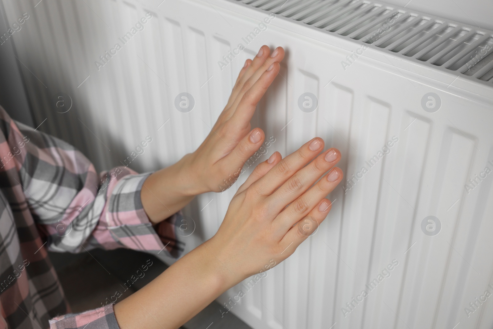 Photo of Woman warming hands on heating radiator near white wall, closeup