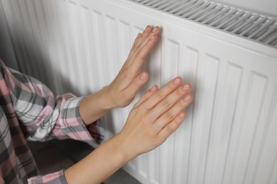 Photo of Woman warming hands on heating radiator near white wall, closeup