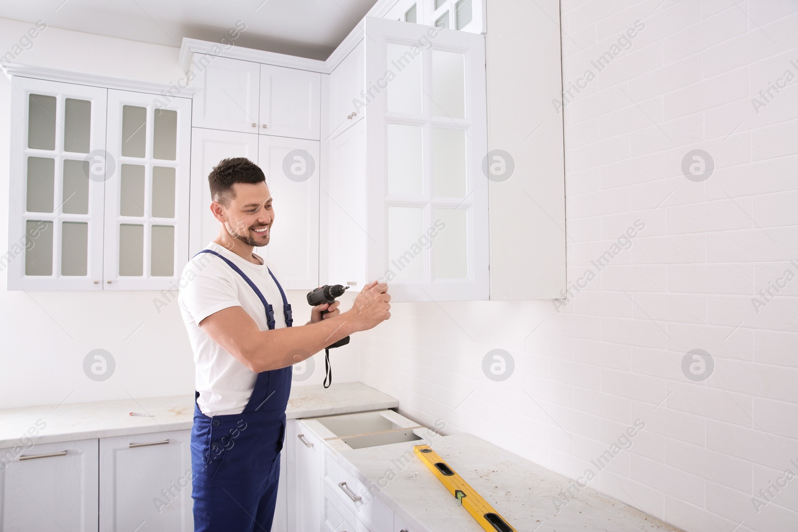 Photo of Worker installing handle on cabinet door with screw gun in kitchen