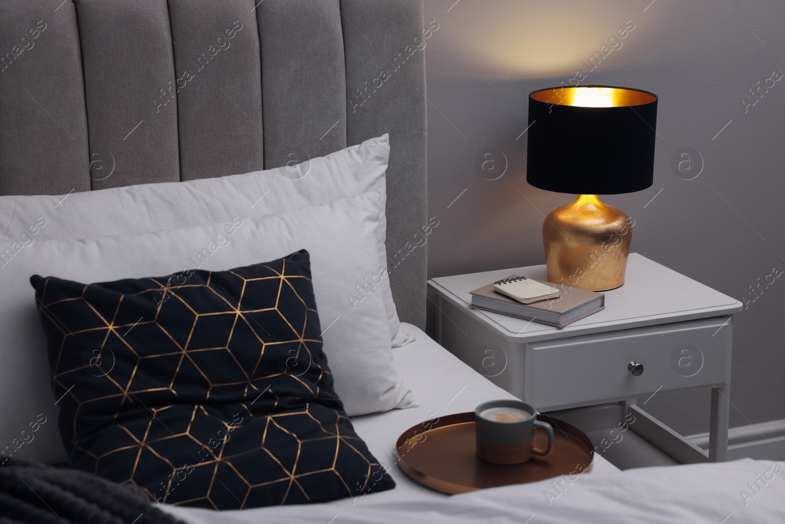 Photo of Stylish lamp and book on bedside table indoors. Bedroom interior element