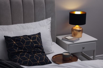 Photo of Stylish lamp and book on bedside table indoors. Bedroom interior element