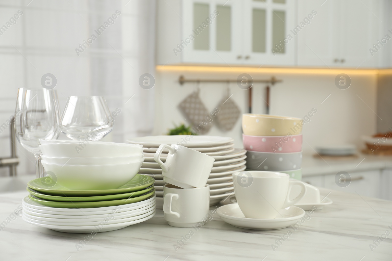 Photo of Clean plates, bowls, cups and glasses on white marble table in kitchen