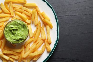 Photo of Plate with french fries and avocado dip on black table, top view. Space for text