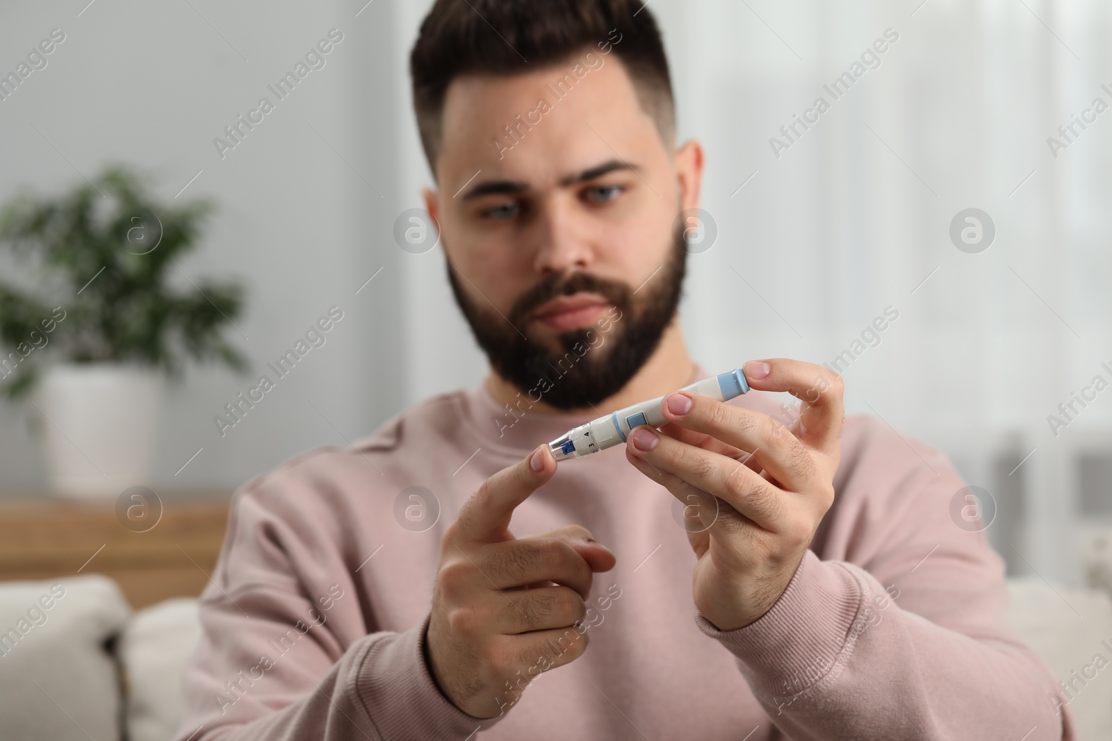 Photo of Diabetes test. Man checking blood sugar level with lancet pen at home, selective focus