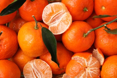 Many fresh tangerines with green leaves as background, top view