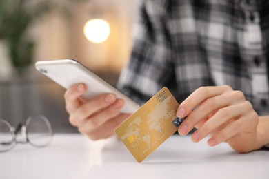 Photo of Woman with credit card using smartphone for online shopping at white table, closeup