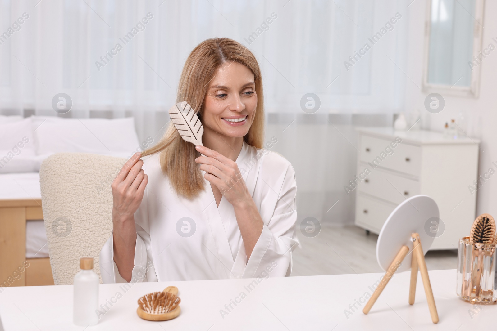 Photo of Beautiful woman brushing her hair at vanity in bedroom