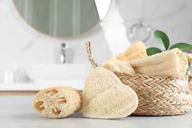 Photo of Natural loofah sponges near wicker basket on table in bathroom