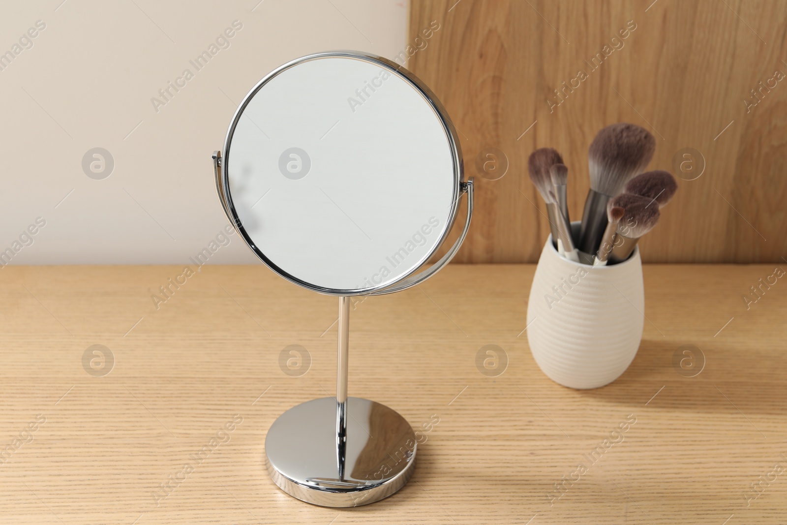 Photo of Mirror and makeup brushes on wooden dressing table in room