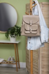 Stylish beige backpack and jacket hanging on clothes rack indoors