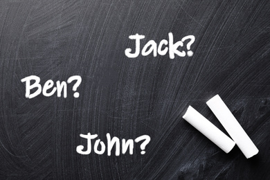 Image of Pieces of white chalk and different baby names written on blackboard, top view