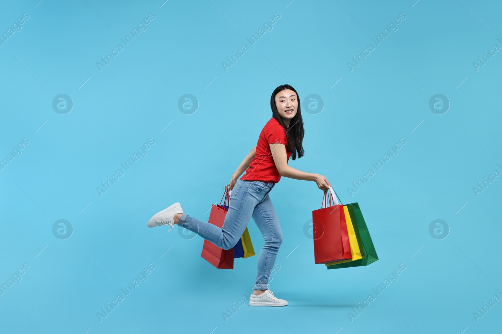 Photo of Happy woman with shopping bags on light blue background