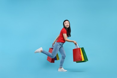 Happy woman with shopping bags on light blue background