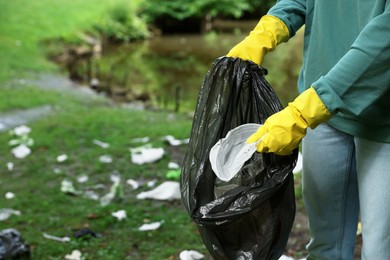 Photo of Woman with plastic bag collecting garbage in park, closeup. Space for text
