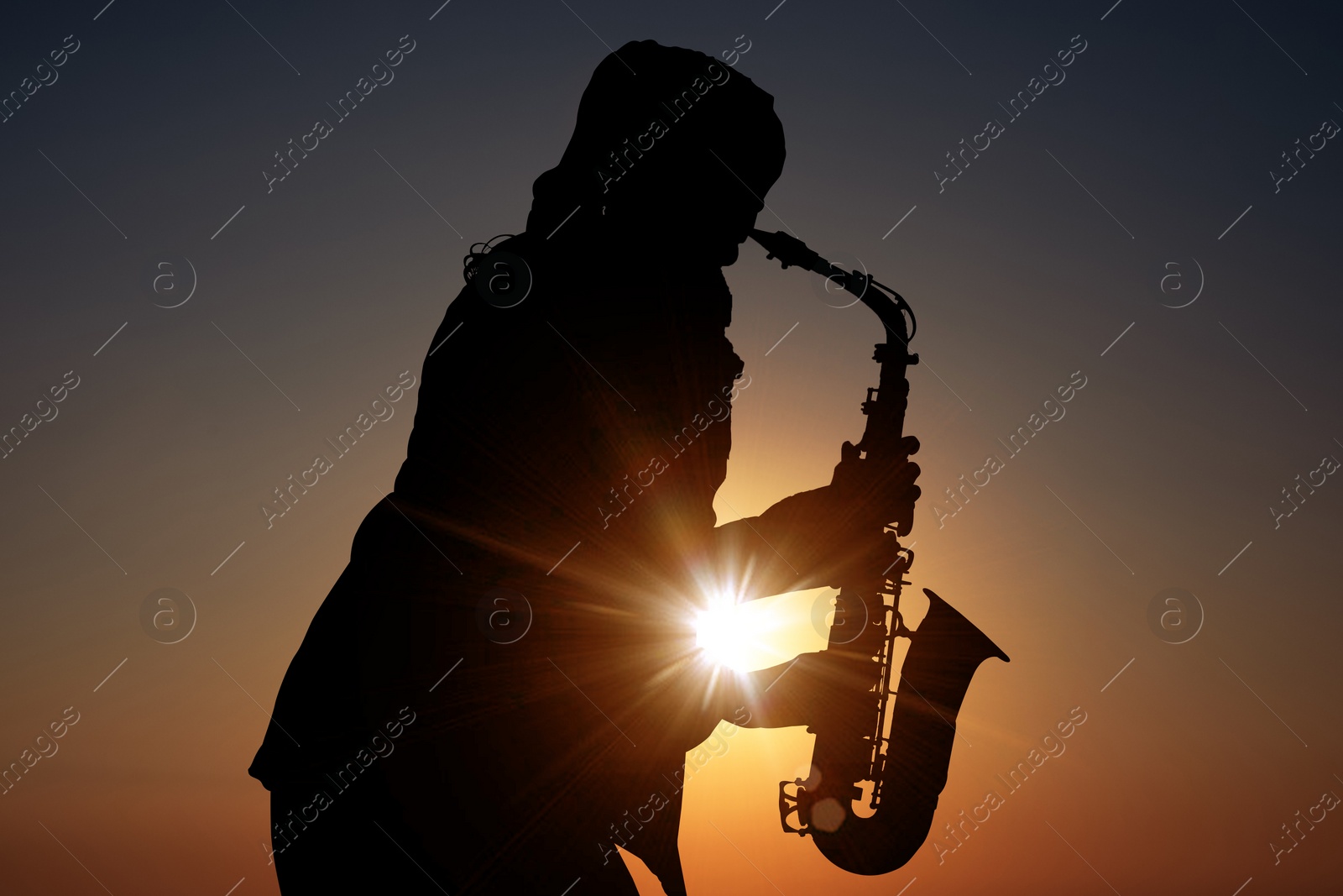 Image of Silhouette of woman playing saxophone against beautiful sky at sunset