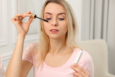 Beautiful woman applying mascara with brush indoors