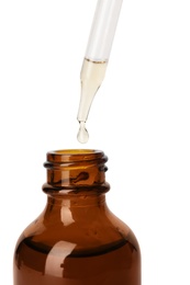 Essential oil dripping from pipette into glass bottle on white background