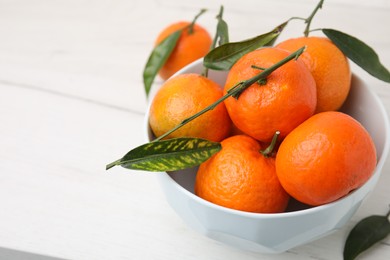 Photo of Bowl with fresh ripe tangerines and leaves on white table, space for text
