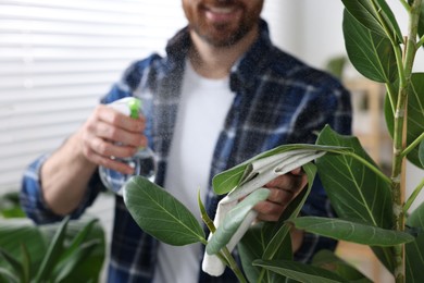 Photo of Man spraying beautiful potted houseplants with water indoors, closeup
