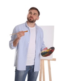 Man with painting tools near easel on white background. Young artist