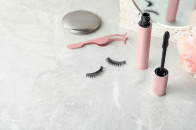 Mascara, fake eyelashes and tweezers on light table, space for text. Makeup product