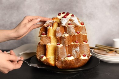 Woman taking slice of delicious Pandoro Christmas tree cake with powdered sugar and berries at black table, closeup
