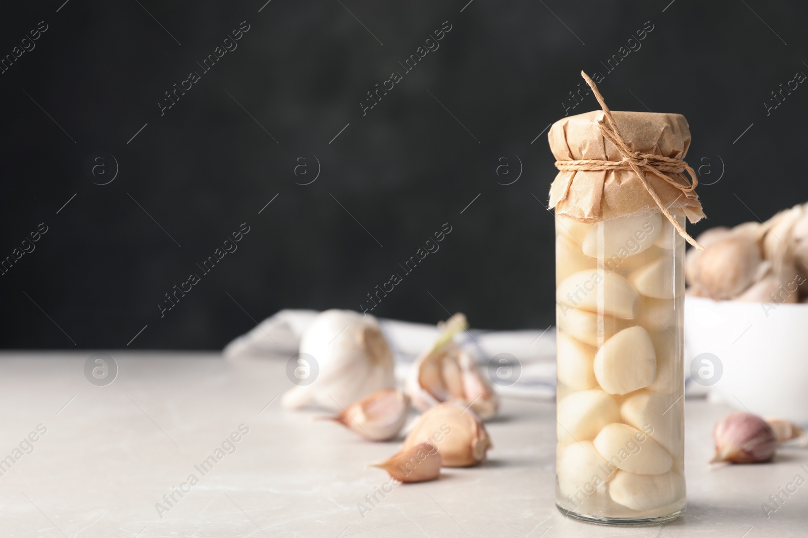 Photo of Preserved garlic in glass jar on table. Space for text