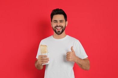Photo of Happy young man with tasty shawarma showing thumb up on red background