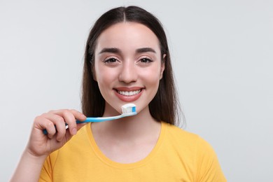 Happy young woman holding plastic toothbrush on white background