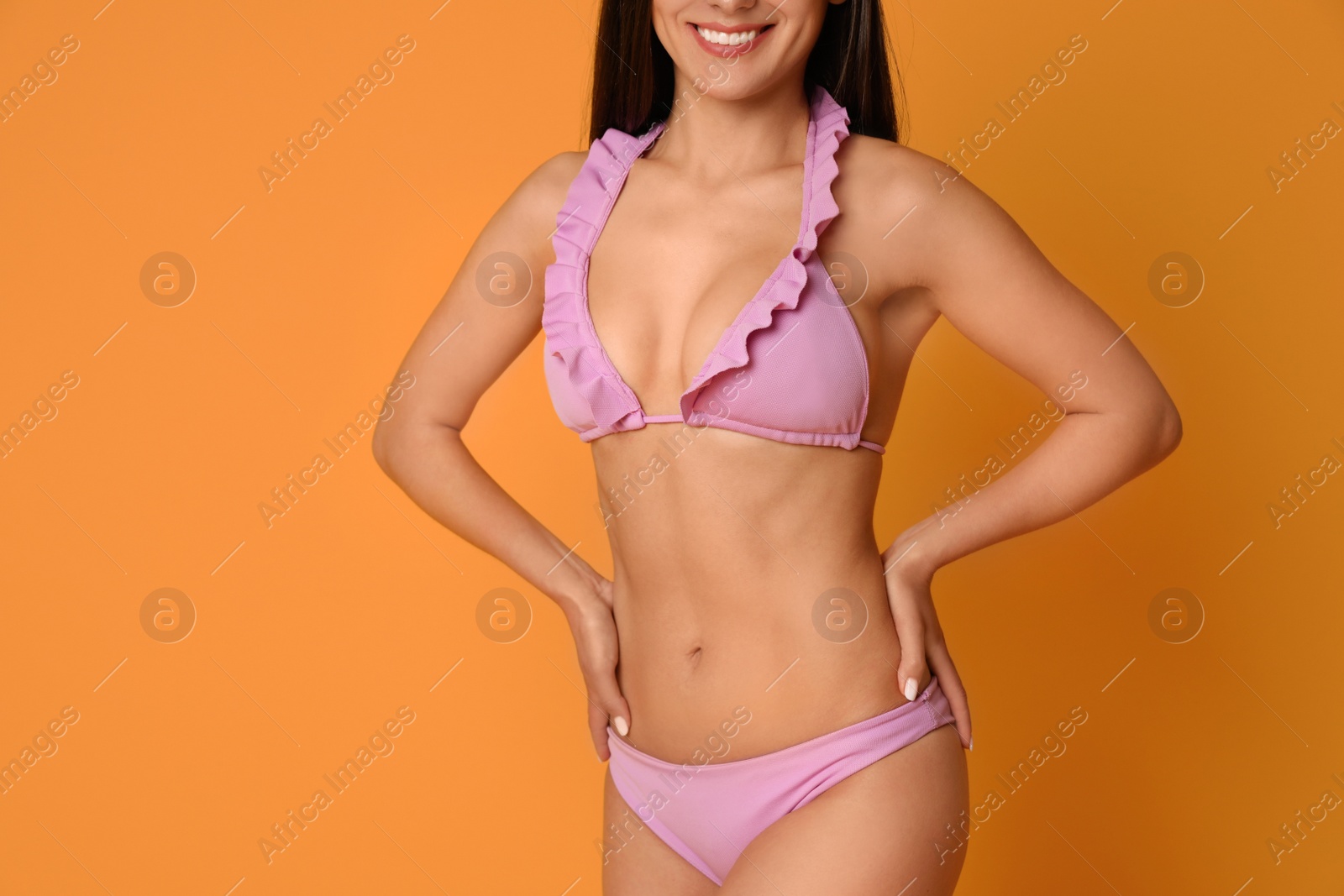 Photo of Pretty sexy woman with slim body in stylish  pink bikini on orange background, closeup view. Space for text