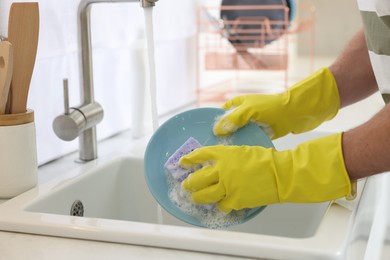 Man washing plate above sink in kitchen, closeup