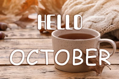 Image of Hello October card. Cup of hot drink and autumn leaves on wooden table