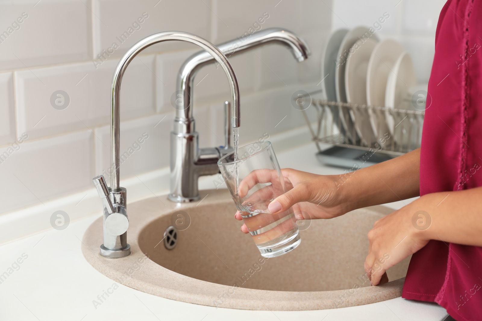 Photo of Woman pouring water into glass in kitchen, closeup