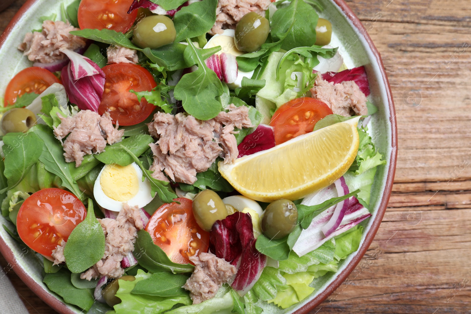 Photo of Plate of delicious salad with canned tuna and vegetables on wooden table, top view