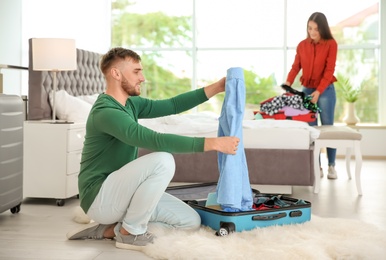 Photo of Young couple packing suitcases for summer journey at home