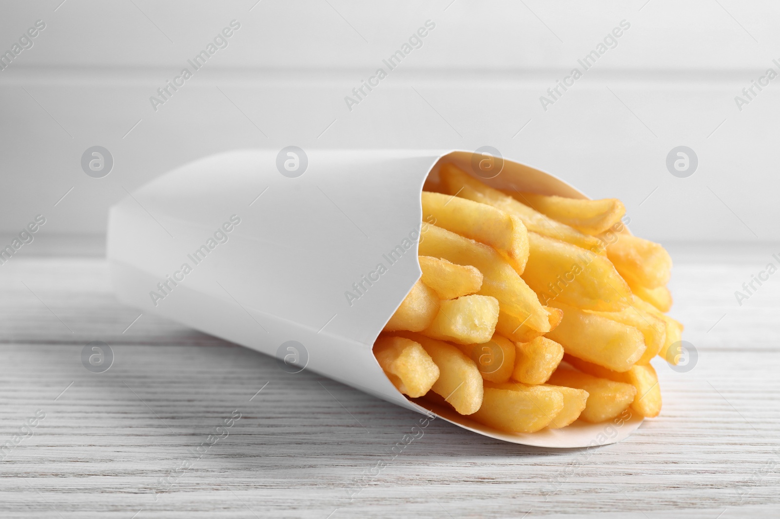 Photo of Delicious french fries in paper box on white wooden table, closeup. Space for text