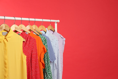 Bright clothes hanging on rack against red background, space for text. Rainbow colors