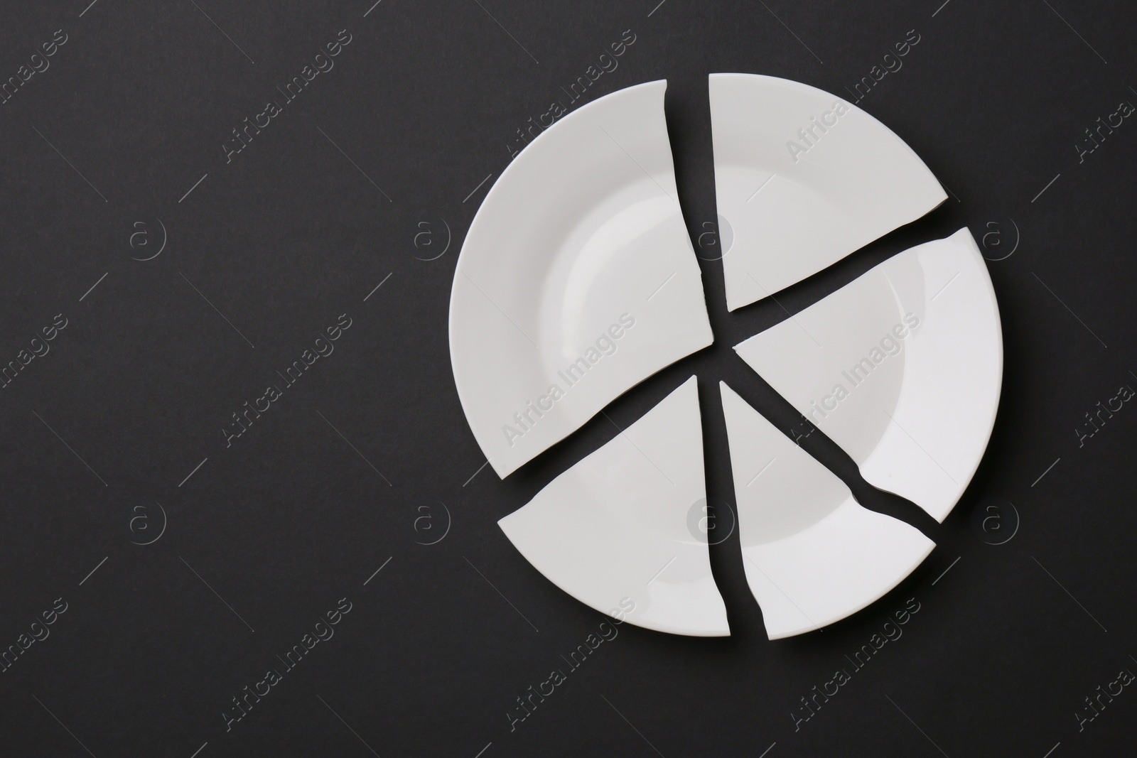 Photo of Pieces of broken white ceramic plate on dark grey background, top view. Space for text