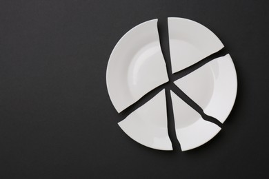 Photo of Pieces of broken white ceramic plate on dark grey background, top view. Space for text