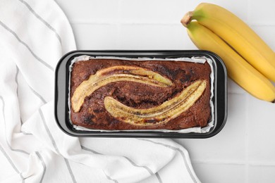 Delicious banana bread and fresh fruits on white tiled table, top view