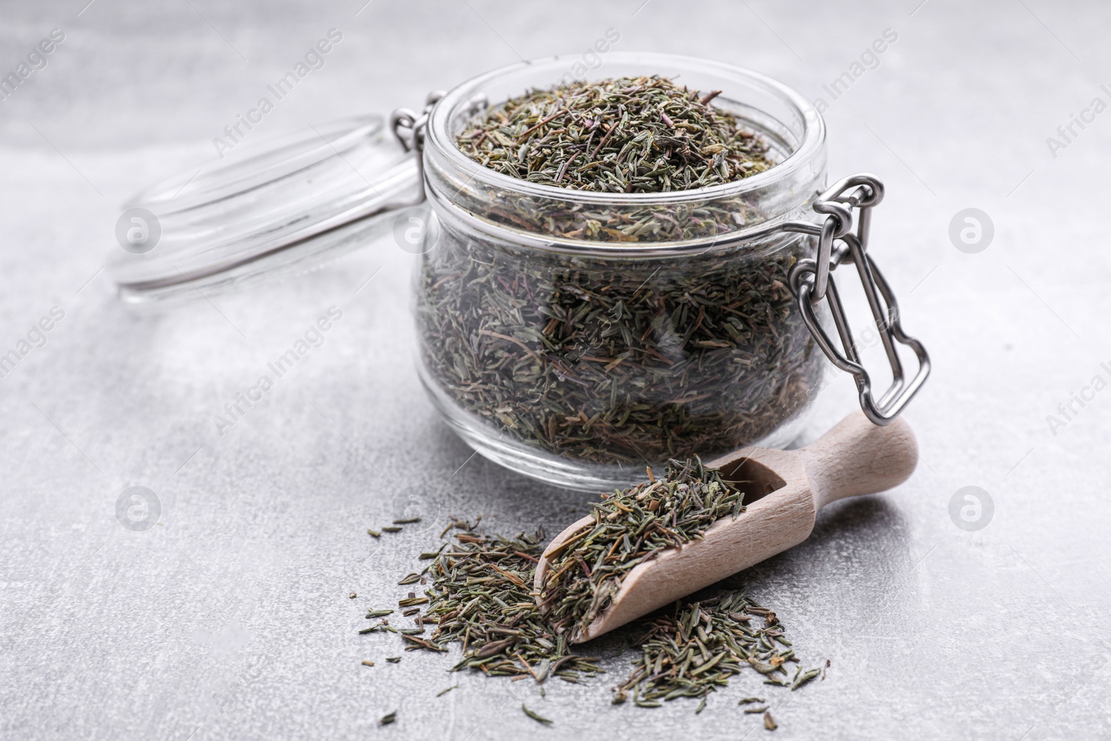 Photo of Jar and scoop with dried thyme on grey table, closeup